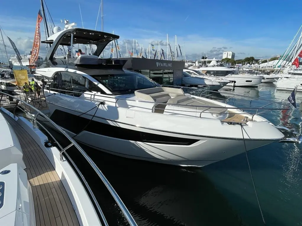 A sleek white motor yacht with a spacious deck is docked at a marina, showcasing luxury boating at a boat show.